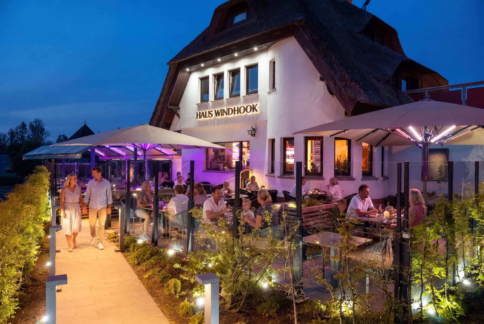 Belebte Restaurant-Terrasse von Haus Windhook am Abend mit Leuchtschrift
